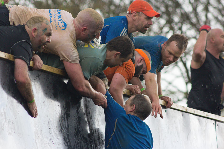 Friends help teammate over and obstacle in UK tough mudder